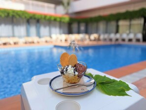 Un postre sobre una bandeja junto a una piscina, con vista clara a la piscina y sillas de descanso al fondo.