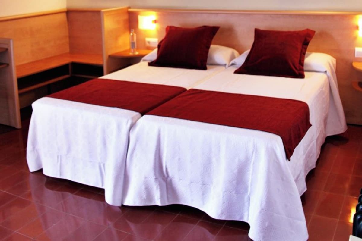 A double bed with white and red bedding, two bedside tables, and wall-mounted lamps.
