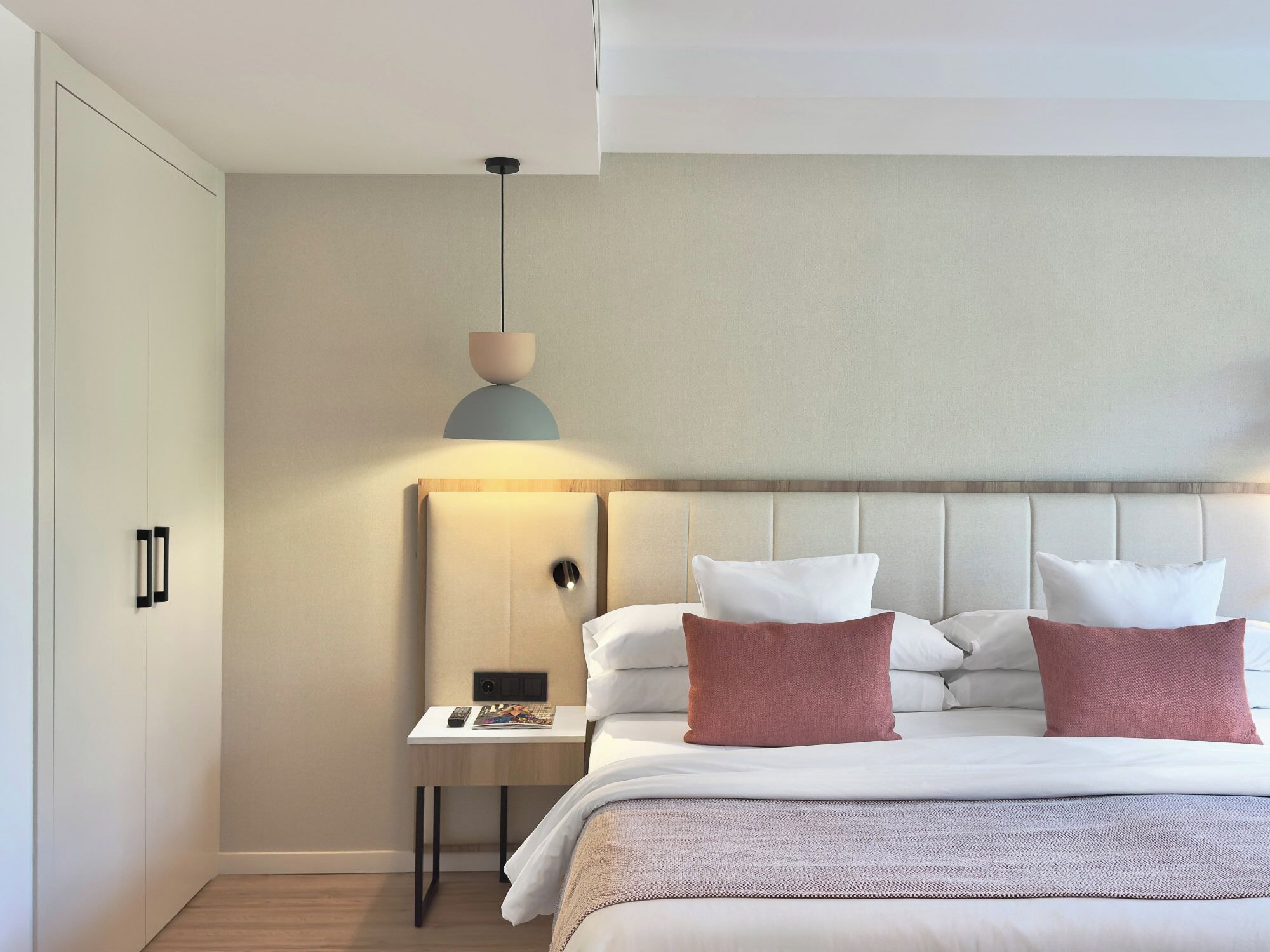 Une chambre d’hôtel moderne avec un grand lit, une table de chevet et un luminaire fixé au mur.