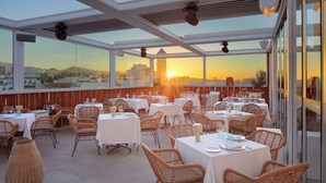 A restaurant with tables and wicker chairs, large windows with a city view, and a ceiling with ventilation. - Obal Hotel Marbella (Marbella)