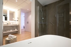 Een moderne badkamer met een douchecabine van glas, een wit bad en een wastafel met spiegel en planken.