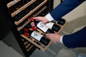 Una persona eligiendo botellas de vino de una estantería de madera.