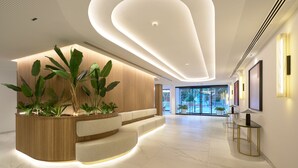 A modern reception area with a curved reception desk, a seating area, and a view of the outdoors through large glass doors. - Obal Hotel Marbella (Marbella)