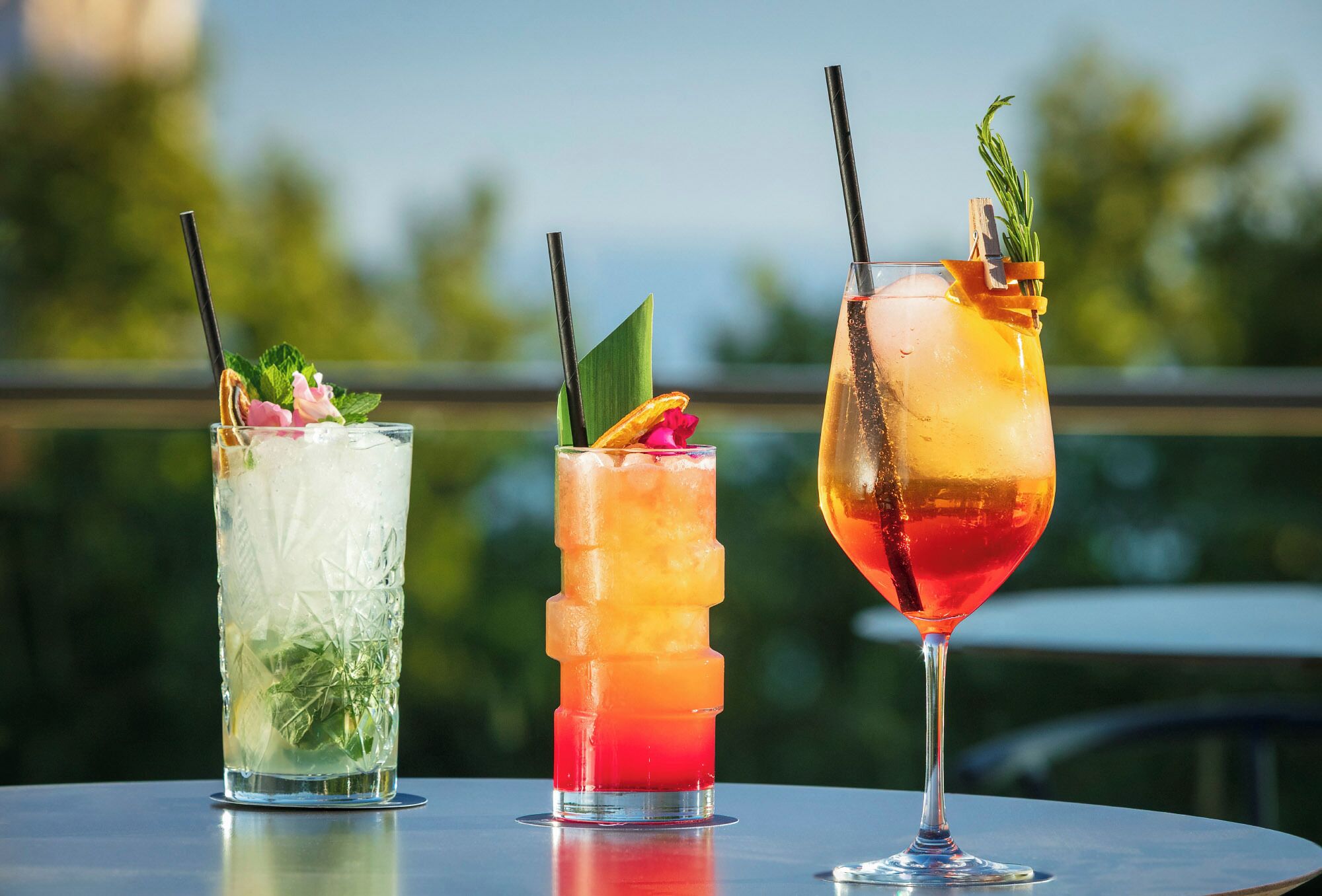 Three cocktails on a table with a view of greenery in the background.