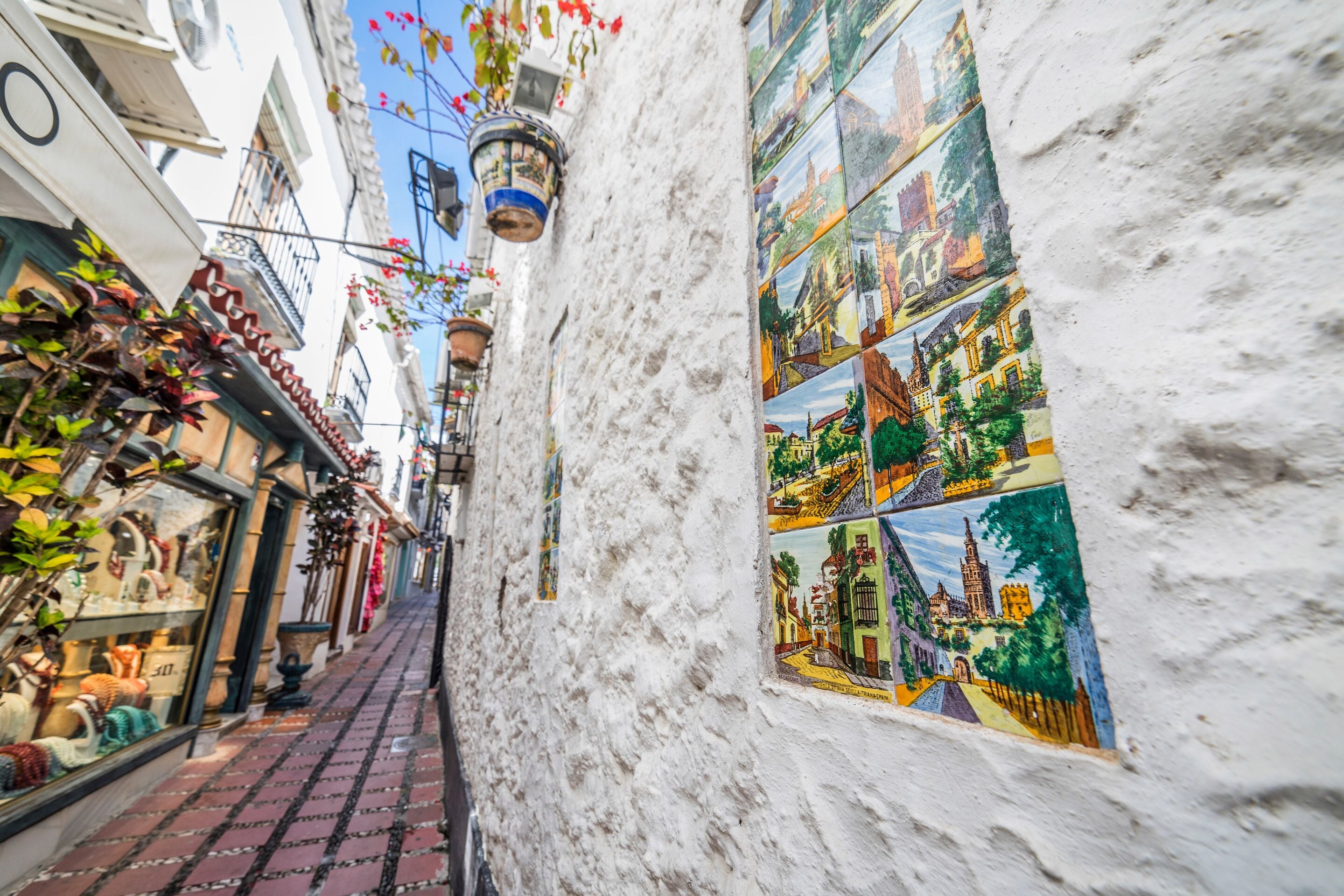 Un estrecho callejón con un muro blanco decorado con mosaicos coloridos que representan diferentes escenas.