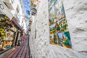 Un estrecho callejón con un muro blanco decorado con mosaicos coloridos que representan diferentes escenas.