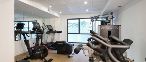 Un gimnasio con máquinas de cardio, una banca y un espejo grande.