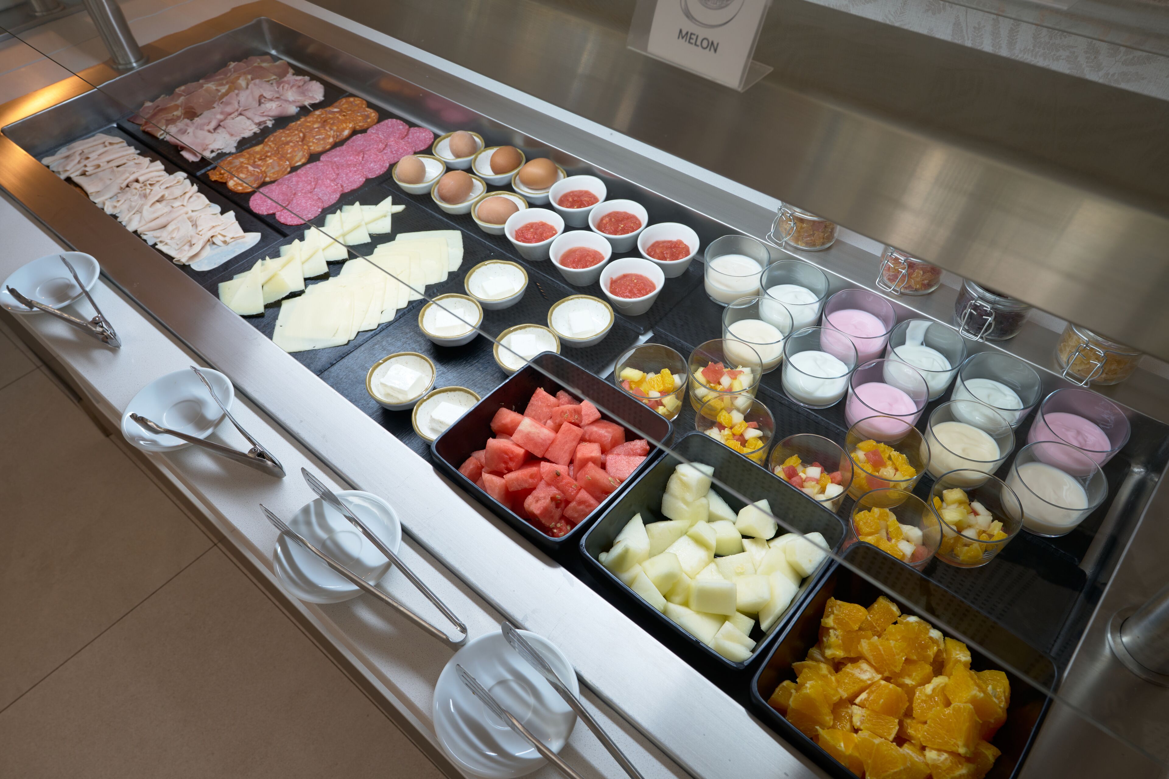 A buffet with various food items including meats, cheeses, fruits, and desserts.