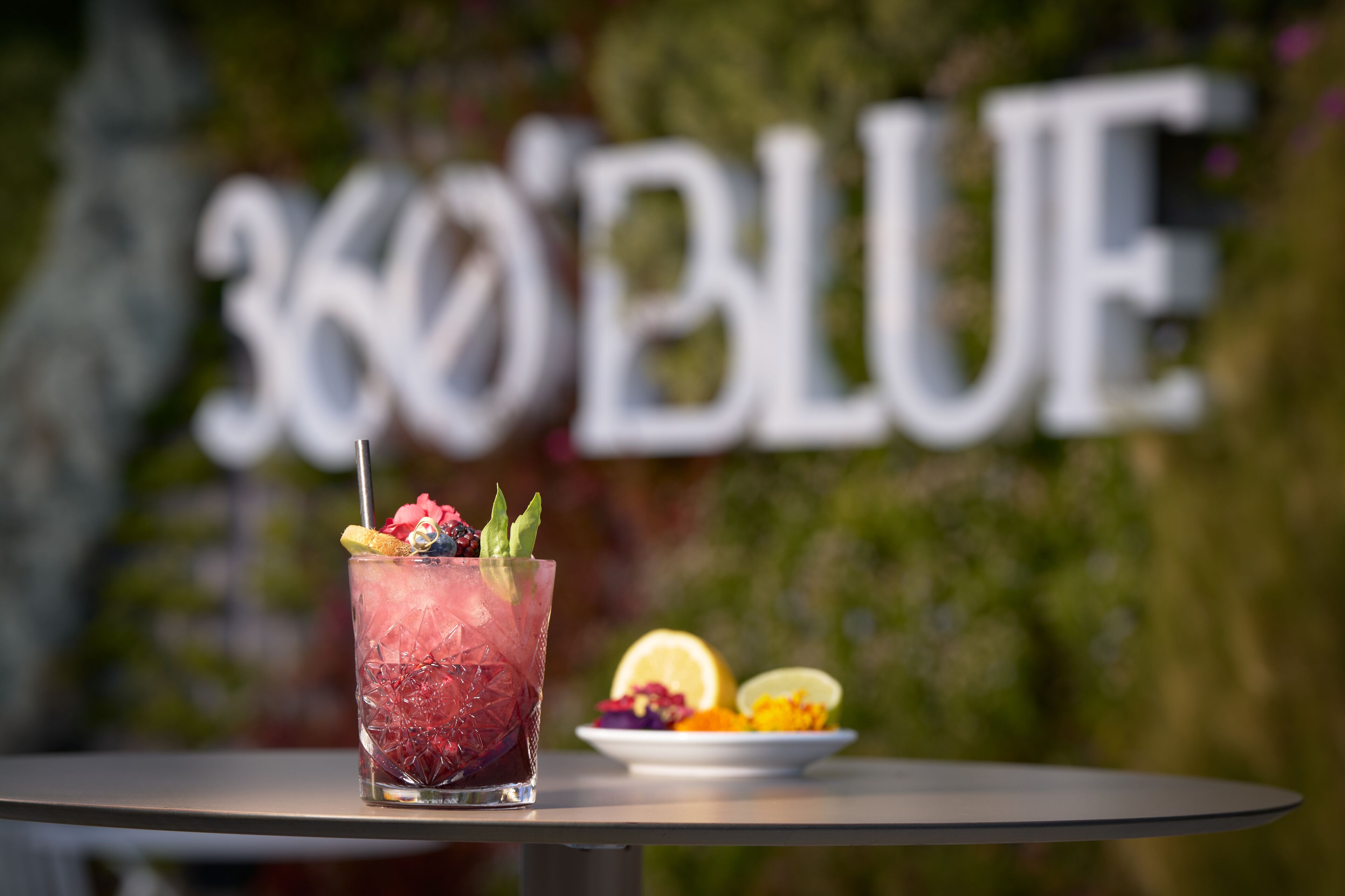 A glass of iced drink with fruit garnish on a table with a blurred background featuring a sign.