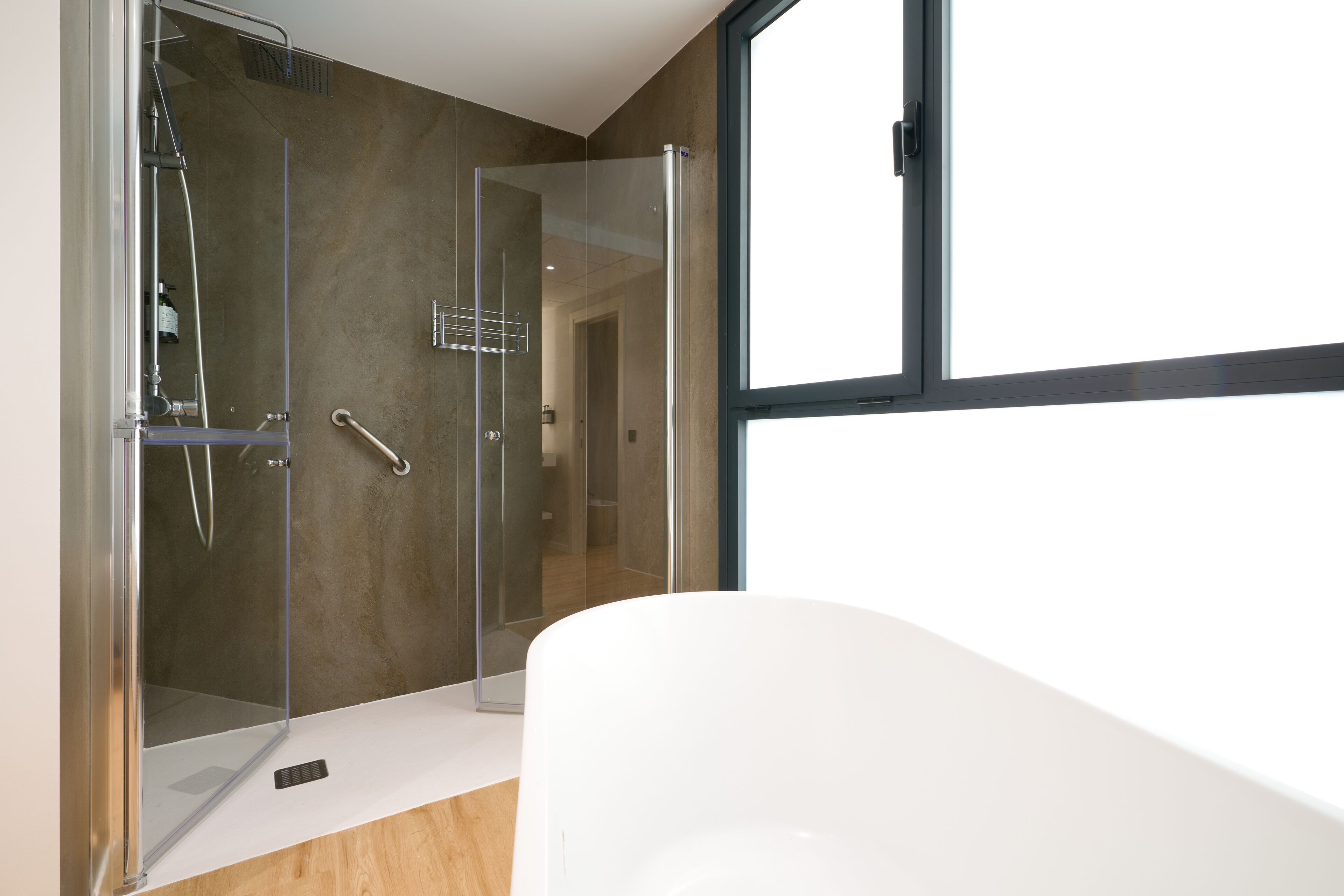 A modern bathroom with a glass-enclosed shower, a white bathtub, and a large window providing natural light.