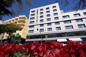 Een modern hotelgebouw met meerdere verdiepingen en balkons, omringd door rode bloemen.