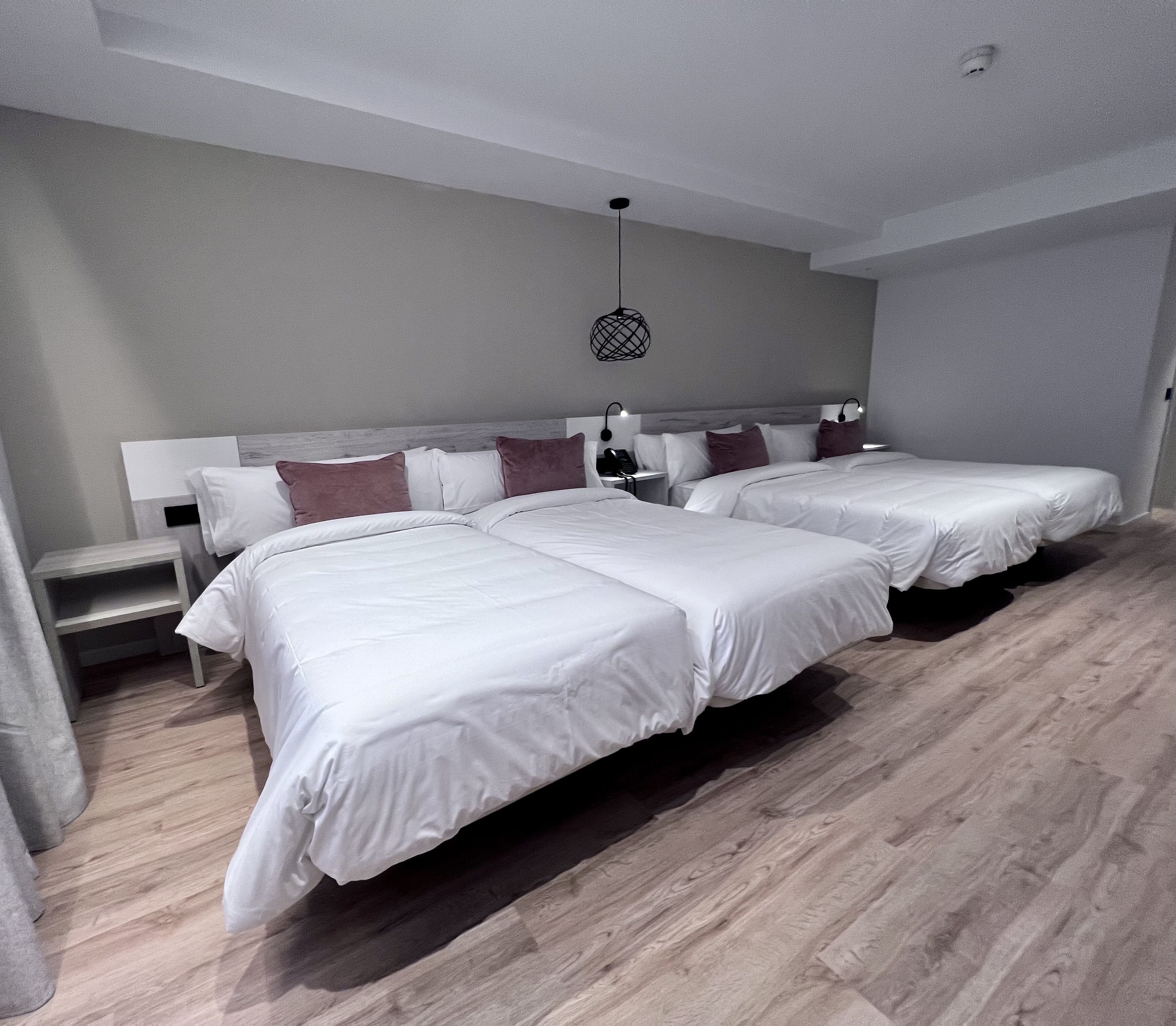 Une chambre d’hôtel moderne avec deux grands lits, une table de chevet, une lampe et un luminaire au plafond.