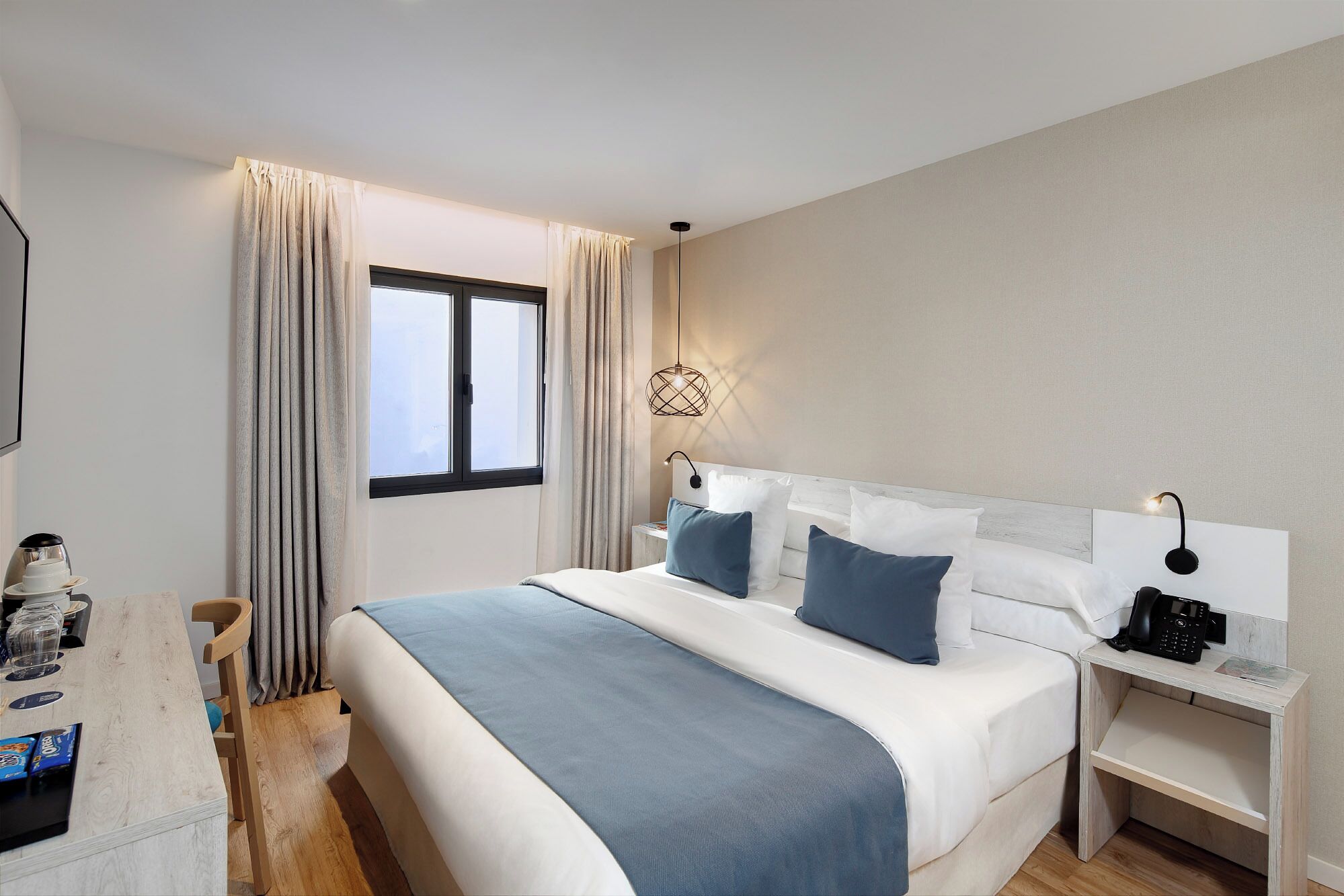 Una habitación de hotel con una cama grande, mesitas de noche, un escritorio con silla y una ventana con cortinas.