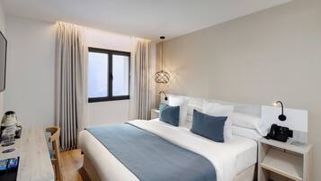 Una habitación de hotel con una cama grande, mesitas de noche, un escritorio con silla y una ventana con cortinas.