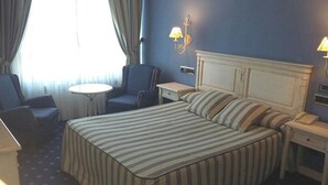A hotel room with a bed, two chairs, a small table, and a bedside telephone. - Hotel Leonor Miron (Soria)