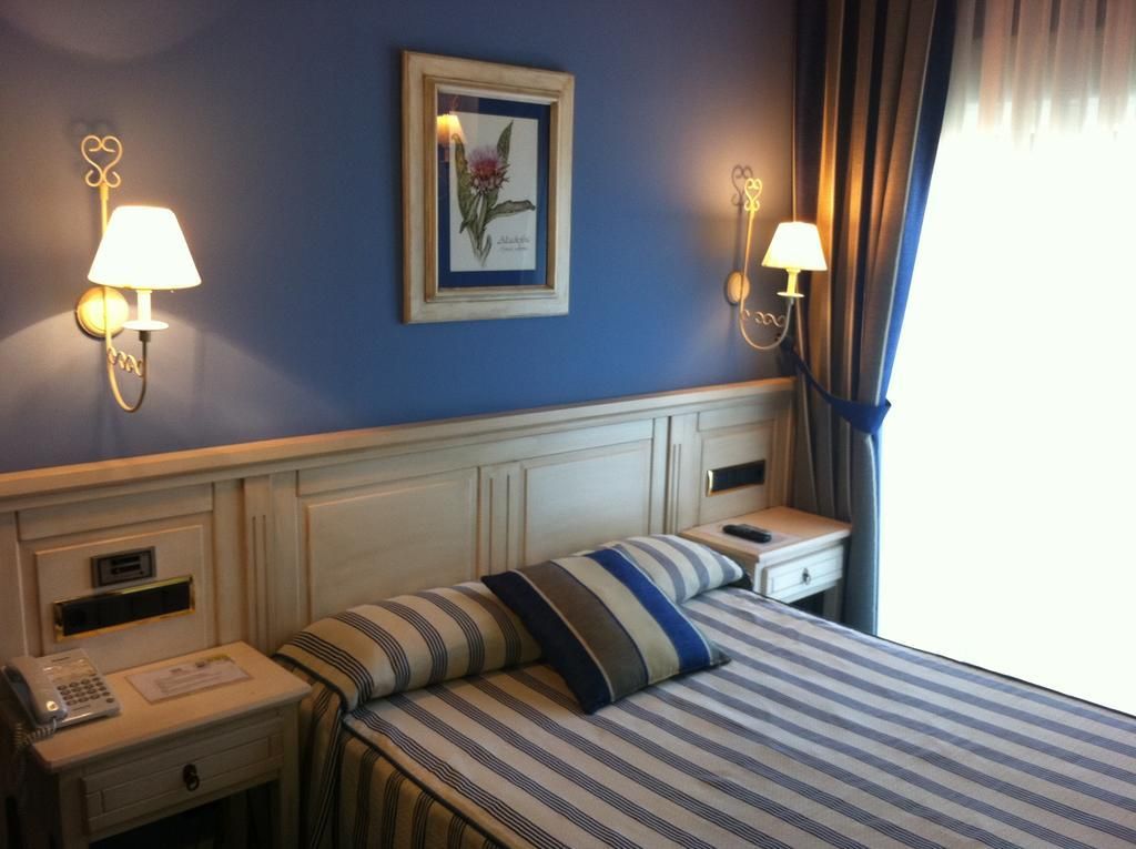 A hotel room with a bed, two bedside tables, a telephone, a lamp, and a framed picture on the wall.