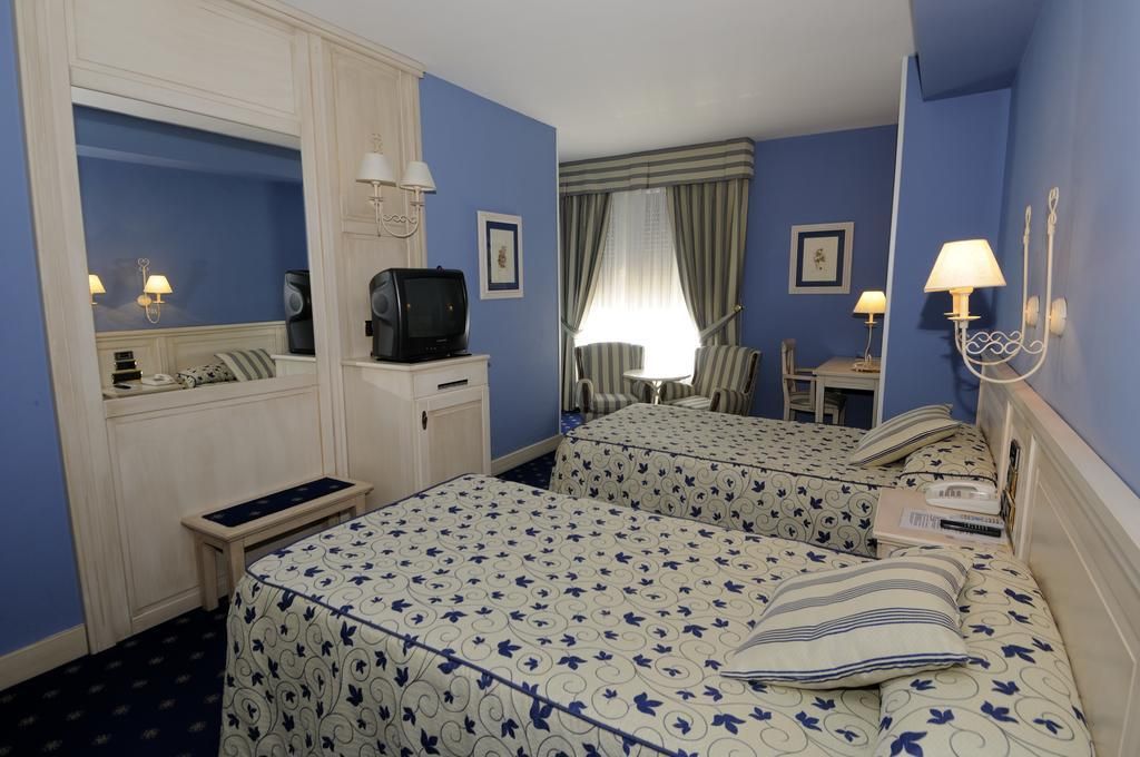A hotel room with two beds, a television, a desk, and a chair.