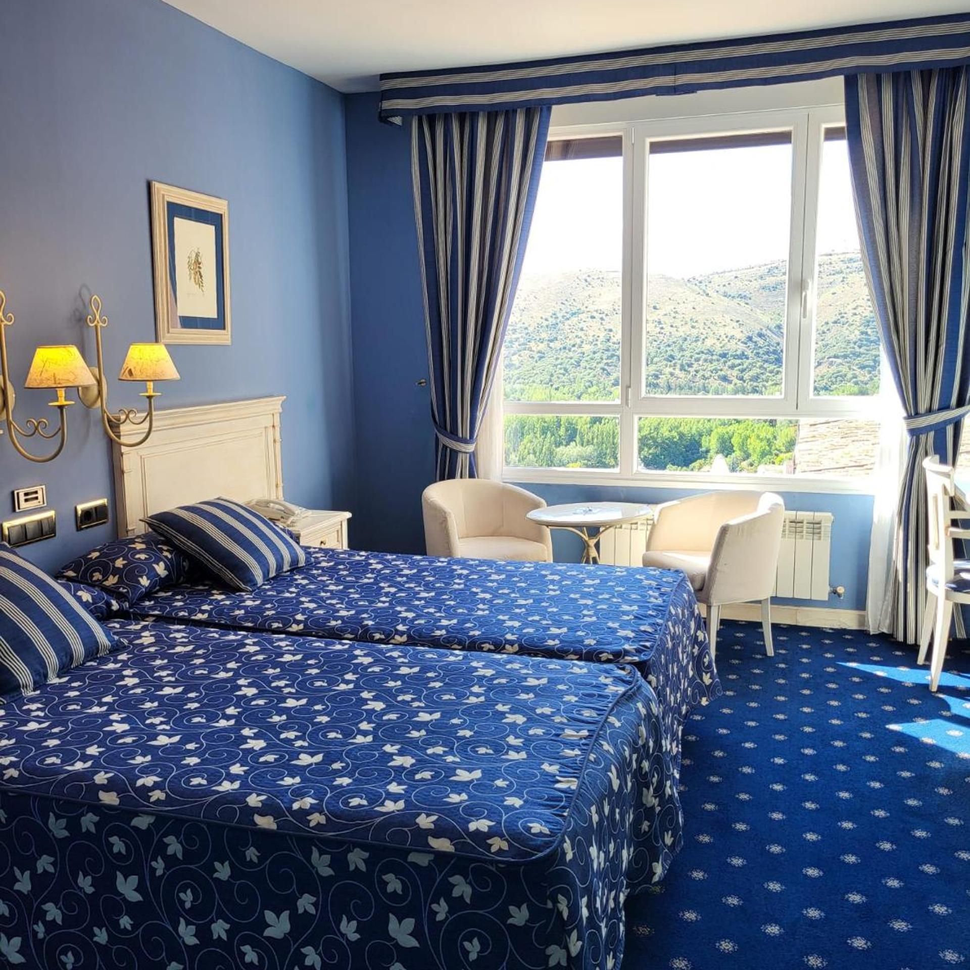 Habitación de hotel con dos camas, una mesita, una silla y vistas al campo.