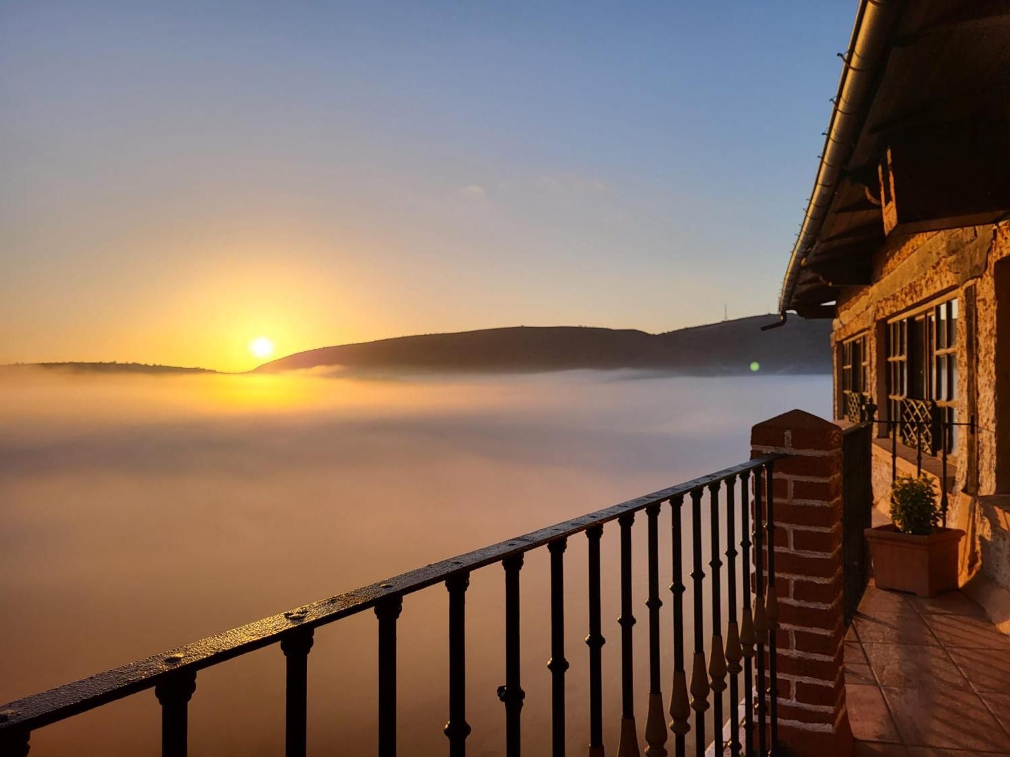 Amanecer sobre un paisaje brumoso con un balcón que domina la vista.