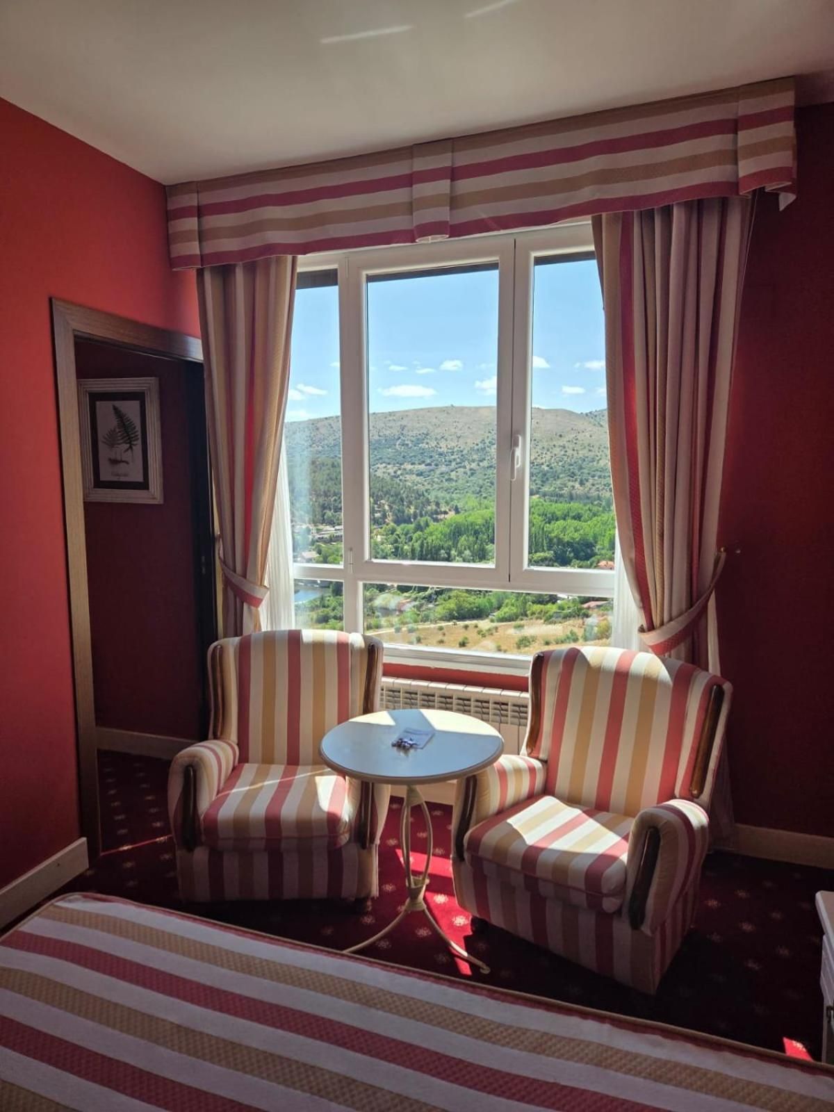 Una habitación con dos sillones a rayas, una mesita redonda y un ventanal con cortinas.
