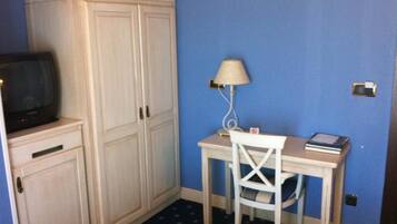 Una habitación con escritorio, silla, lámpara, televisor y armarios.