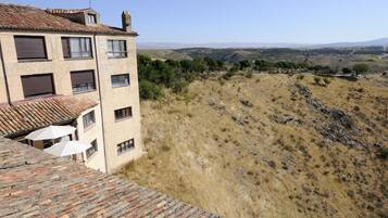 A building with multiple windows and a tiled roof, overlooking a hilly landscape with sparse vegetation.
