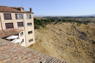 Un edificio con varias ventanas y techo de tejas, con vistas a un paisaje montañoso y vegetación escasa.