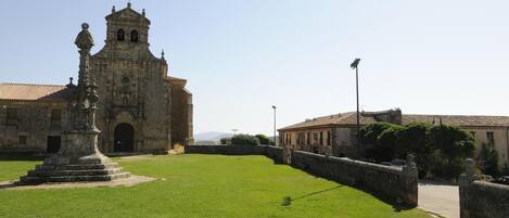 Un edificio histórico con un campanario, un patio con una estatua y un muro de piedra.