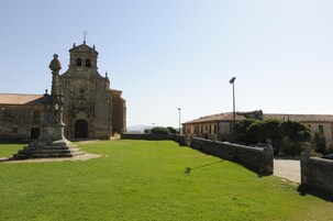 Un edificio histórico con un campanario, un patio con una estatua y un muro de piedra.