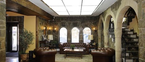 Un amplio vestíbulo con pared de piedra, sofás de cuero, una mesa de centro y una escalera con barandilla de piedra.