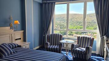 Habitación de hotel con una cama grande, dos sillones, una mesita y vistas a un paisaje montañoso.