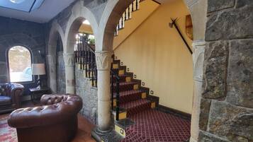 A spacious lobby with a stone column, a leather sofa, and a staircase leading to an upper level.