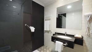 A modern bathroom with a walk-in shower, a large mirror, a sink, and a hairdryer on the wall.
