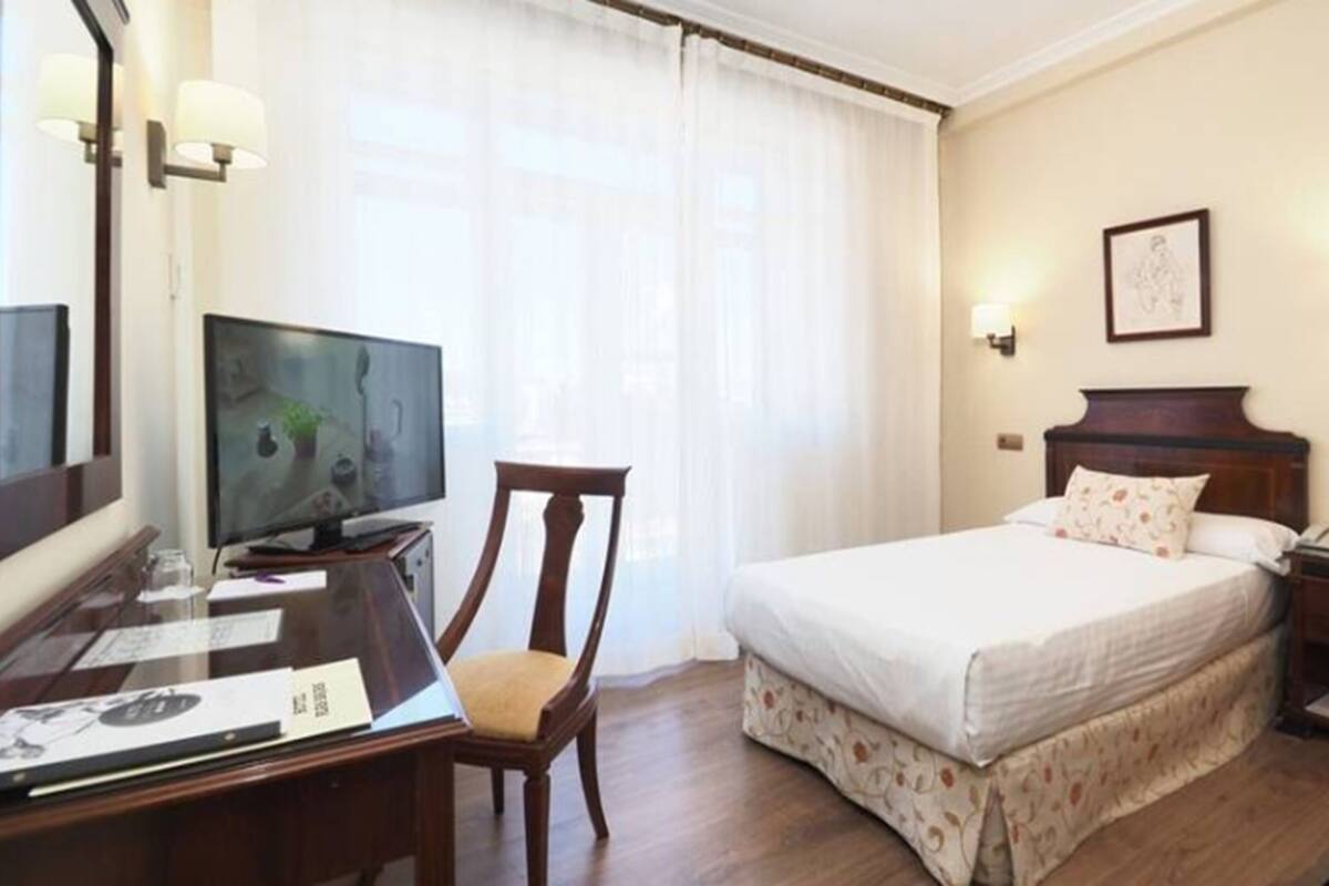 A hotel room with a bed, a desk with a computer, a chair, and a television.