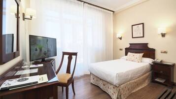Una habitació d'hotel amb llit, escriptori amb ordinador, cadira i televisió.