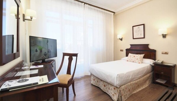 A hotel room with a bed, a desk with a computer, a chair, and a television.