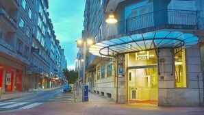 A hotel with a glass facade, a covered entrance, and a street view with other buildings and shops.