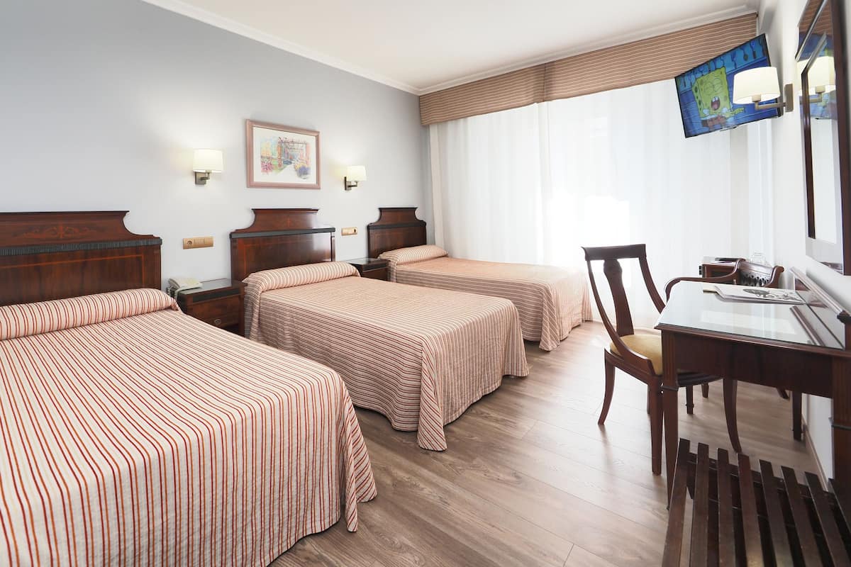 A hotel room with two beds, a desk with a chair, a television, and a window with curtains.
