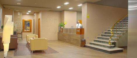 A hotel lobby with a reception desk, a staircase, and seating area.