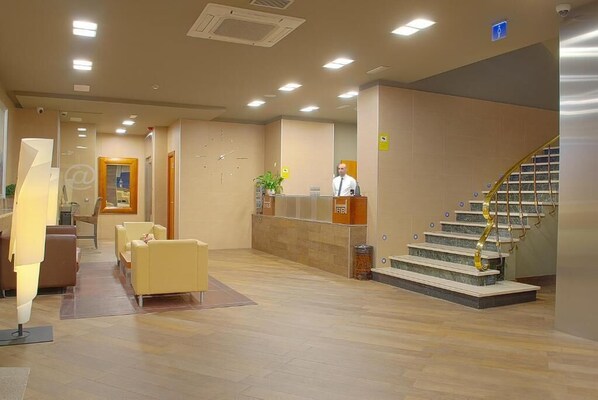 A hotel lobby with a reception desk, a staircase, and seating area.