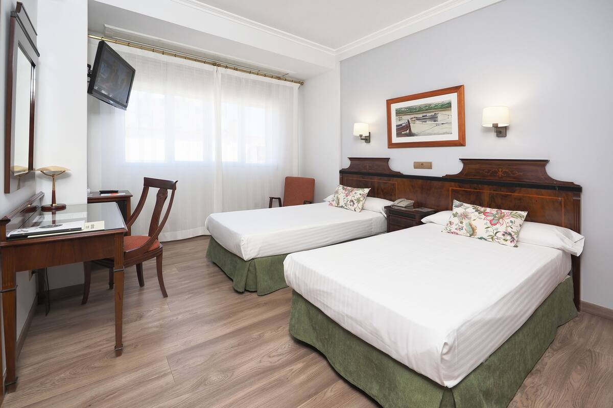 A hotel room with two beds, a desk, a chair, a television, and a painting on the wall.