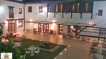 Un patio con mobiliario exterior, una fuente y un área cubierta con mesas y sillas.
