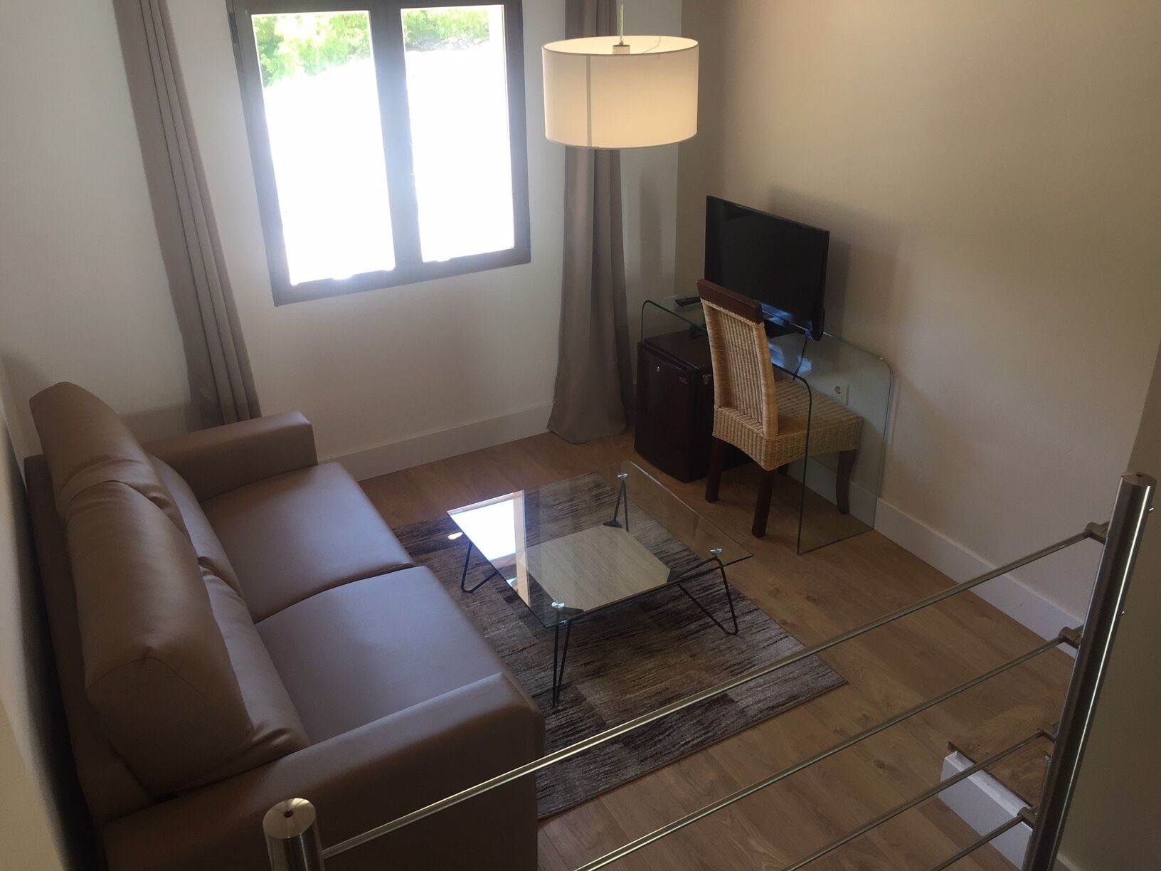 Una sala de estar moderna con un sofá de cuero marrón, una mesa de centro de vidrio, un televisor sobre un mueble bajo y una lámpara.