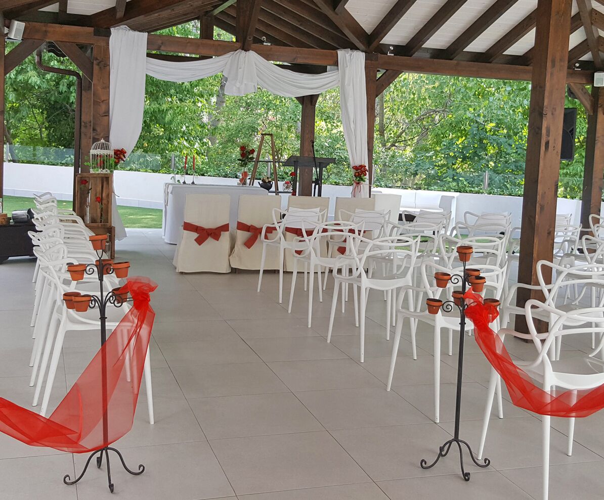Un espacio para eventos al aire libre con sillas y mesas blancas, lazos rojos y un toldo blanco.