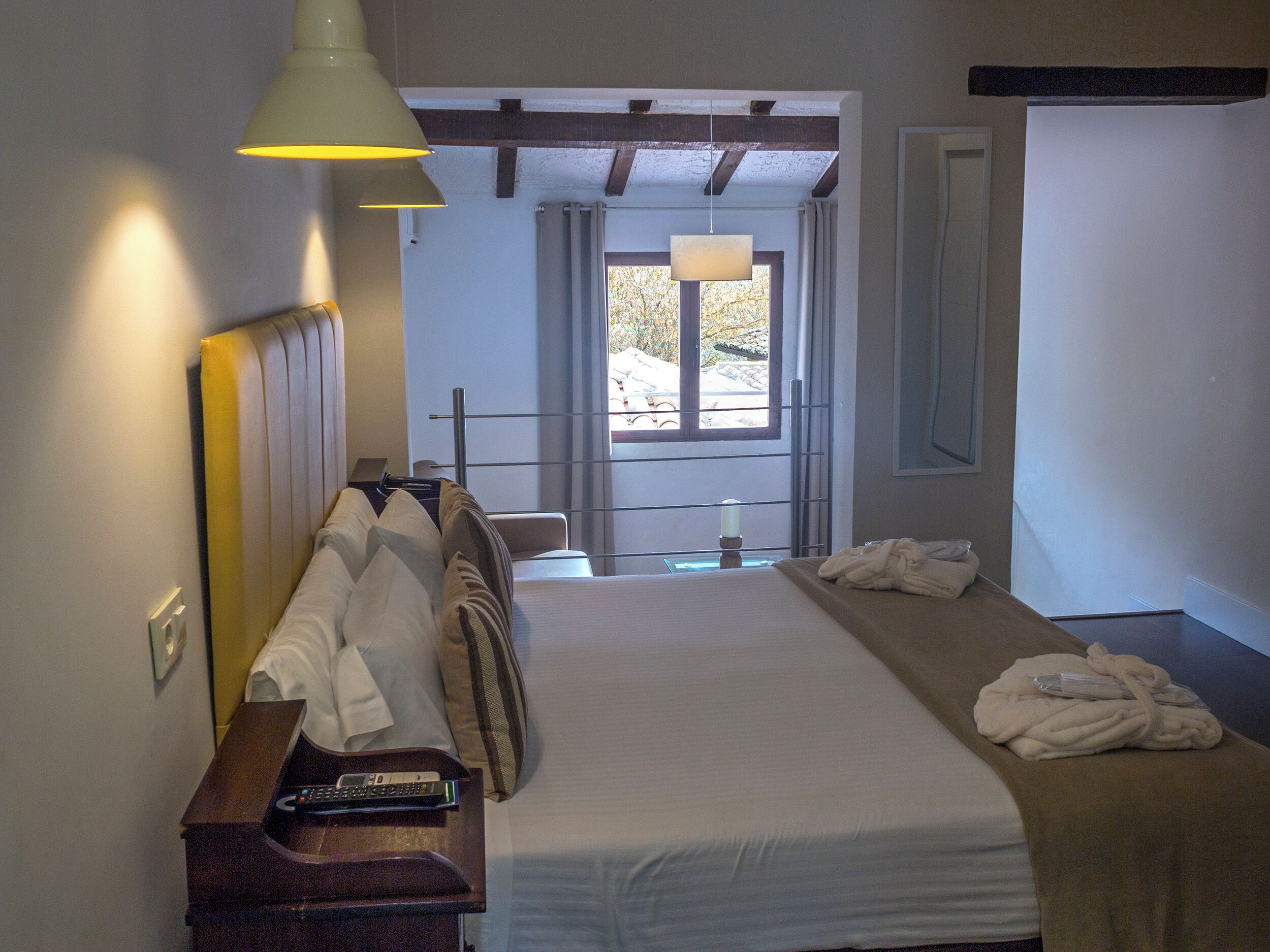 Een hotelkamer met een bed, nachtkastje, lamp en uitzicht op het omliggende landschap.