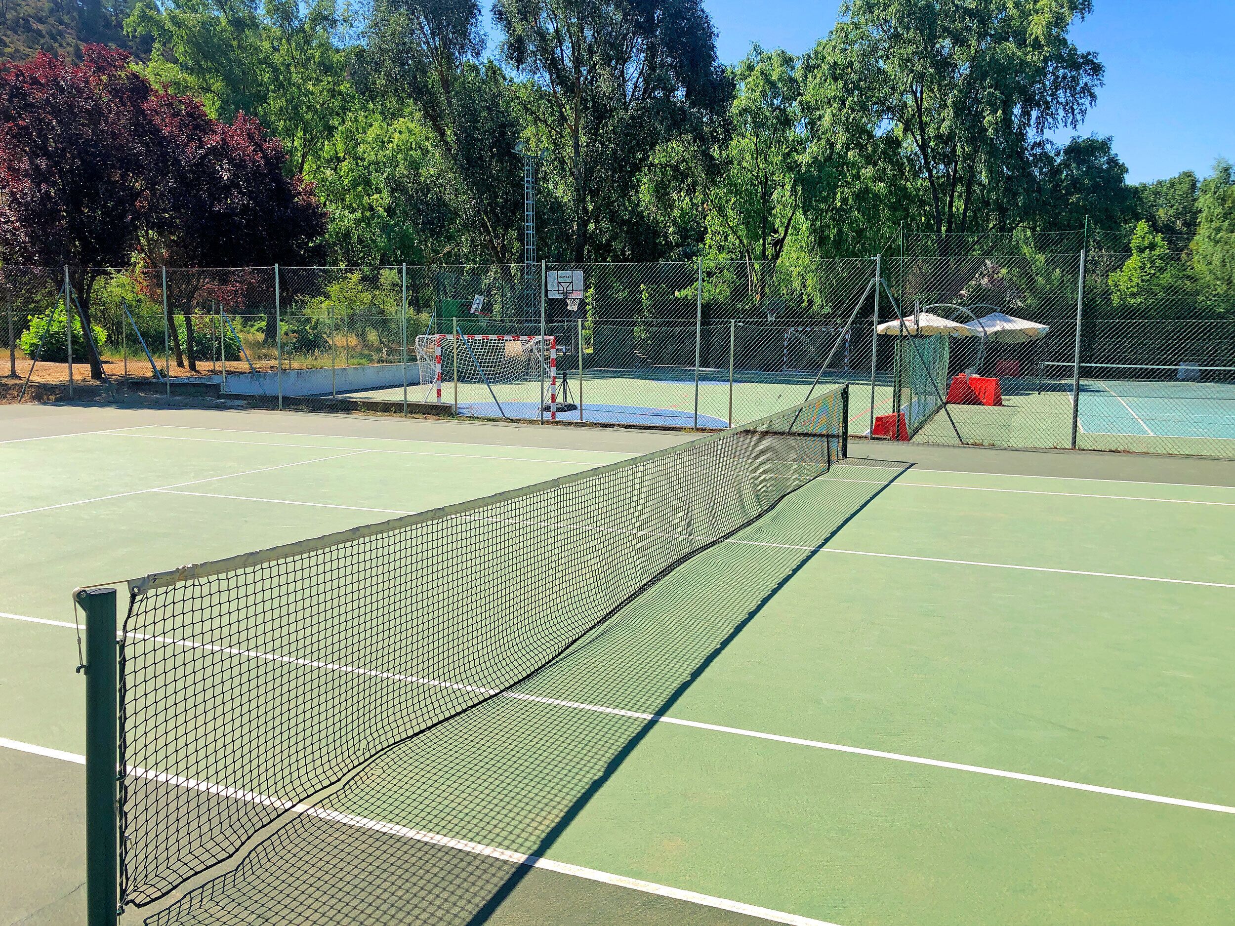 A tennis court with a net, surrounded by a fence and trees.