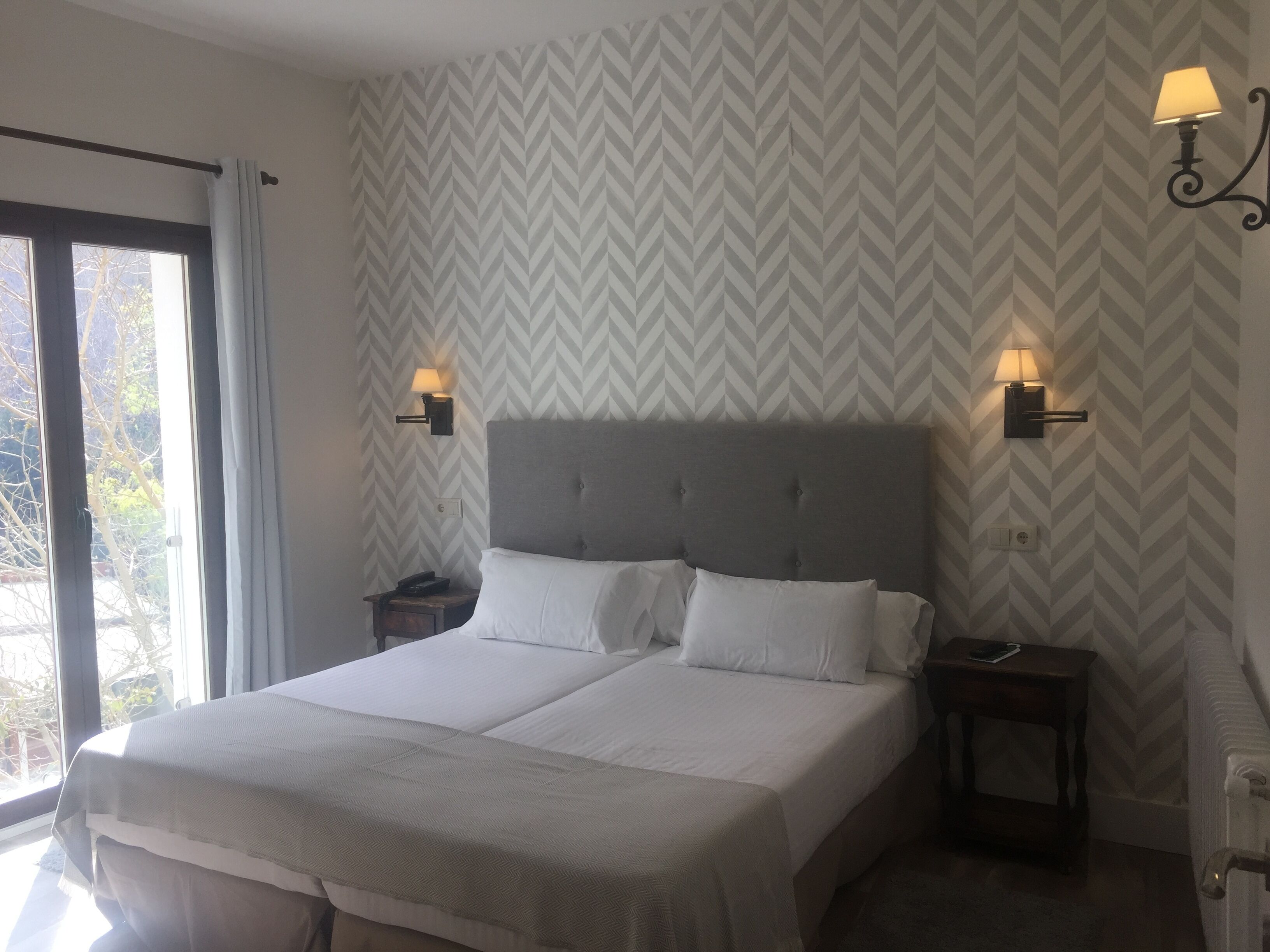 A double bed with two bedside tables, each with a lamp, in a room with a chevron-patterned wallpaper.