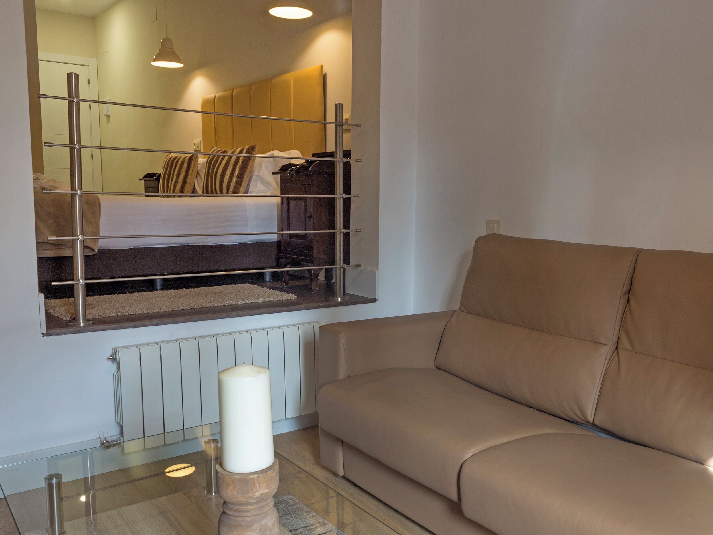 A modern living room with a glass coffee table, a beige sofa, and a bed with a headboard.