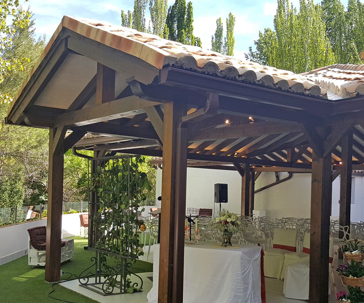 Un espacio al aire libre techado con una estructura de pérgola, mesas dispuestas para comer y un sistema de sonido.