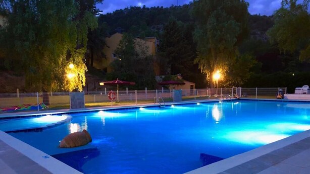 Ein rechteckiger Pool mit einer Fliesenverkleidung, umgeben von einem Zaun, beleuchtet durch Overhead-Lampen.